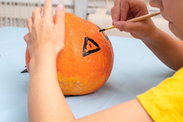 Disegnare a mano una faccia spaventosa su una zucca arancione con un pennello per creare una lanterna di Halloween Jack, primo piano. Sfondo di festa di Halloween e stile di vita familiare