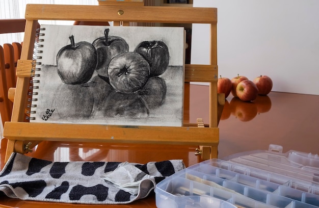 Disegnare frutta con carboncino quattro mele su un blocco per schizzi su un cavalletto portatile