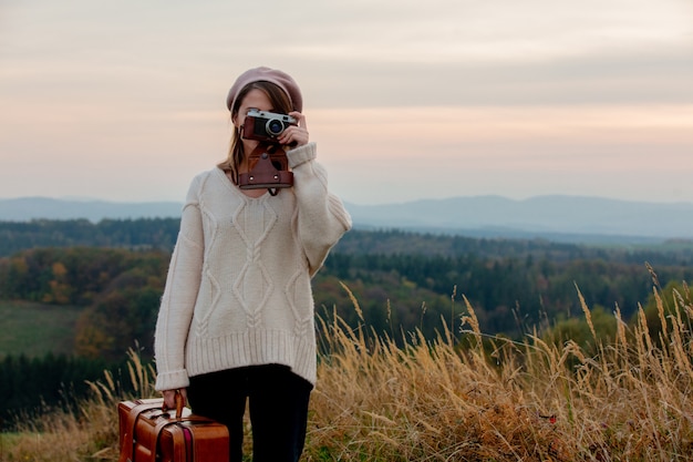 Disegni la donna con la macchina fotografica della foto e della valigia alla campagna con le montagne