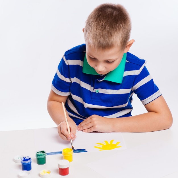 Disegno allegro felice del bambino con la spazzola in album facendo uso di molti strumenti della pittura. Concetto di creatività.