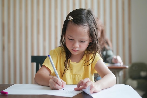 Disegno del bambino della ragazza in età prescolare con la matita di colore su carta bianca sul tavolo in aula con gli amici