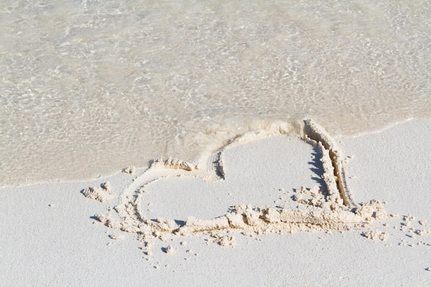 Disegno del cuore sulla spiaggia con l'onda.