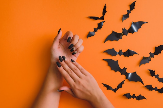 Disegno di arte del chiodo di Halloween. Posa piatta con pipistrelli e bella manicure sulle mani su sfondo arancione