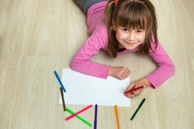 Disegno sveglio della ragazza del bambino con i pastelli variopinti delle matite su Libro Bianco. Educazione artistica, concetto di creatività.