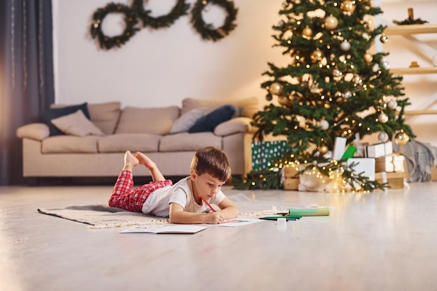 Disegno usando la matita Il ragazzino è nella stanza con l'albero di Natale è sul pavimento