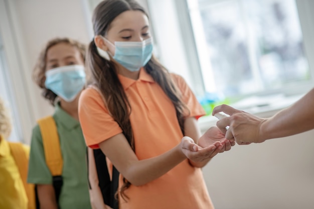 Disinfettante. Ragazza dai capelli scuri con maschera preventiva che si prende un disinfettante in mano