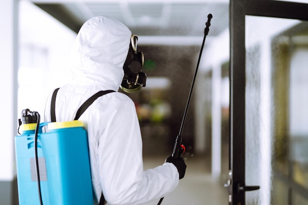 Disinfezione dell'ufficio per prevenire COVID-19, uomo in tuta protettiva ignifuga con prodotti chimici spray.