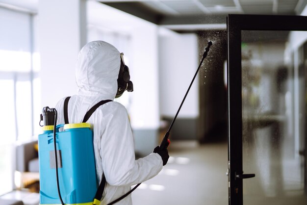 Disinfezione dell'ufficio per prevenire COVID19 Uomo in tuta protettiva ignifuga con prodotti chimici spray
