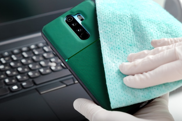 Disinfezione della tastiera del telefono e del laptop con disinfettante alcolico. La donna in guanti pulisce il telefono con tessuto e disinfettante durante il covid 19. Protezione prevenzione dell'igiene da infezioni, germi, batteri