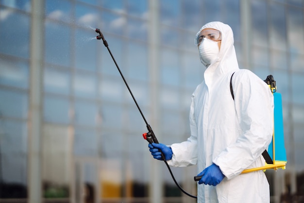 Disinfezione per prevenire COVID-19, uomo in tuta protettiva ignifuga con spray.