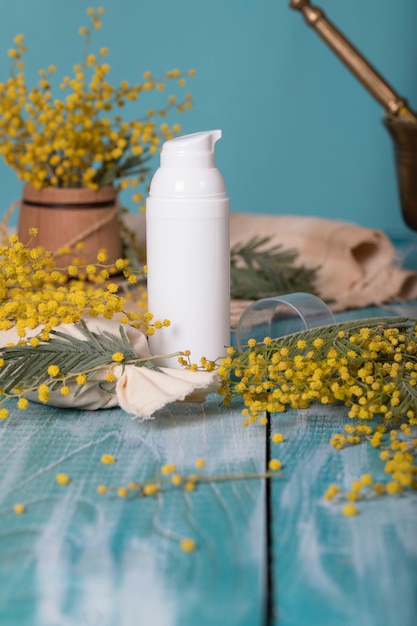 Dispenser crema viso Mimosa su piano in legno ciano. Avvicinamento