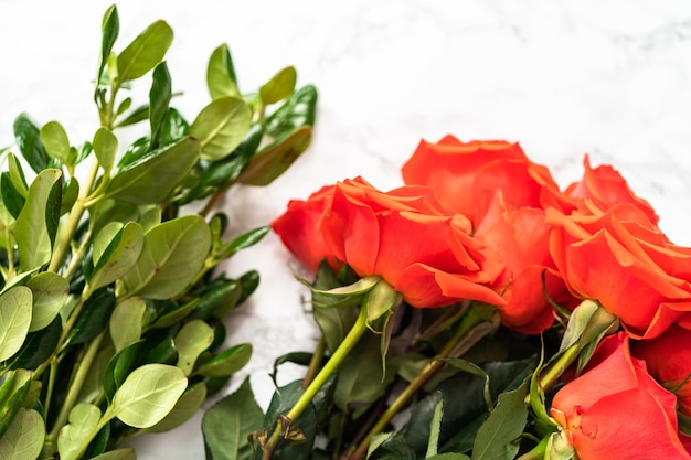 Disporre rose rosse e foglie verdi in un bouquet su fondo marmoreo.