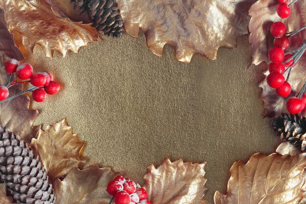 Disposizione autunnale dorata. Foglie di quercia metalliche, pigne e bacche rosse incorniciano una superficie lucida.