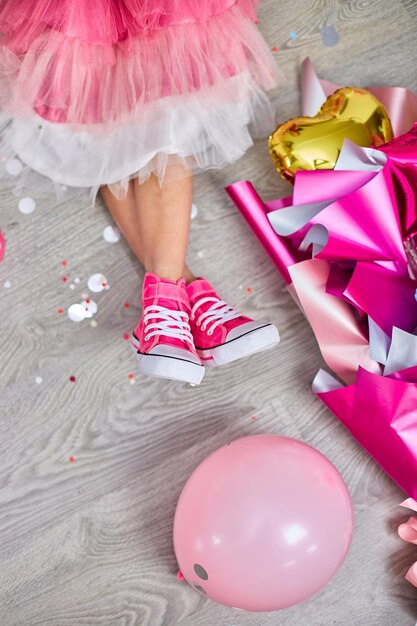 Disposizione creativa della gamba funky della ragazza in scarpe da ginnastica rosa e abito composizione di compleanno piatta Spazio di copia Concetto di festa di compleanno