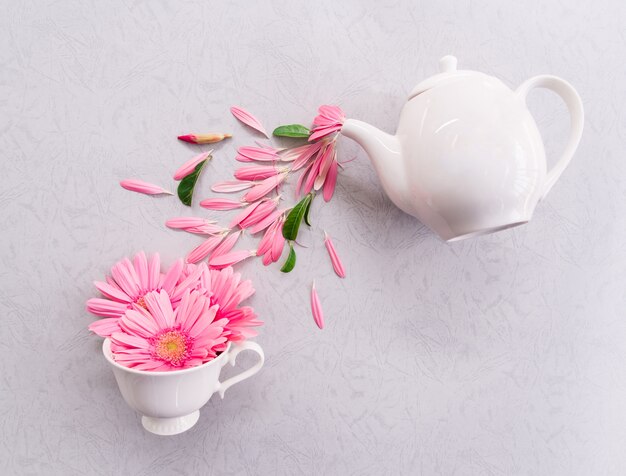 Disposizione creativa fatta della tazza e del vaso di caffè con i fiori dentellare su priorità bassa grigia.