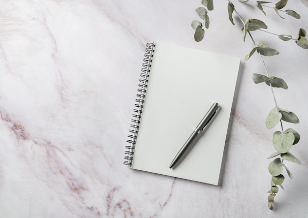 Disposizione dell'area di lavoro dell'home office con una penna bianca per notebook e fiori secchi su sfondo di marmo rosa Vista dall'alto e spazio per la copia