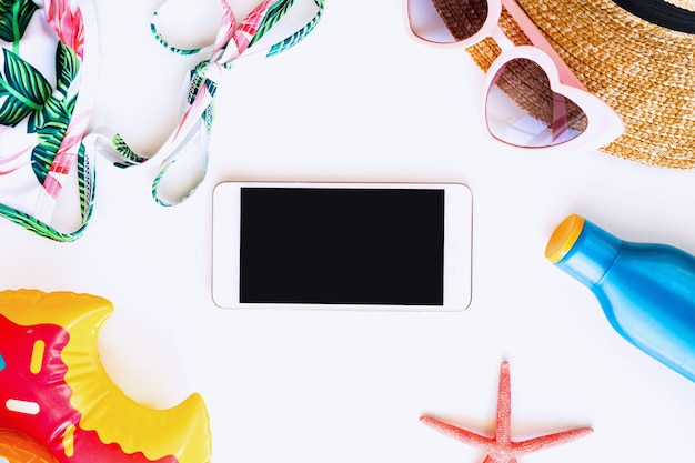 Disposizione piana degli accessori di estate e dello smartphone dello schermo in bianco per lo spazio isolato, vista superiore della copia. Concetto di vacanza tropicale.
