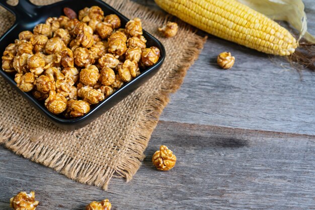 Disposizione piana del popcorn saporito del caramello in piatto di pentola ceramico nero con le tovaglie del sacco e del mais sulla tavola di legno, fine su.