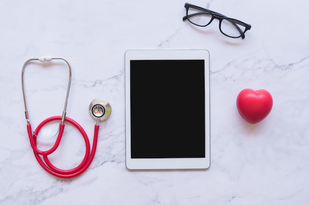 Disposizione piana di buon concetto sano, cuore rosso e stetoscopio e compressa su fondo di marmo bianco