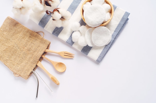 Disposizione piana di prodotti sostenibili, cucchiaio di legno, paglia inossidabile e cotone naturale su bianco