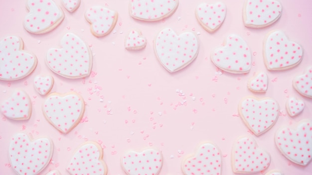 Disposizione piatta. Biscotti di zucchero a forma di cuore decorati con glassa reale su sfondo rosa.