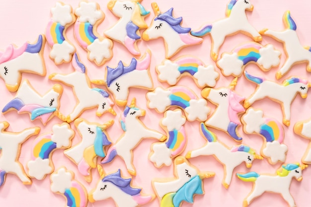 Disposizione piatta. biscotti di zucchero unicorno decorati con glassa reale e glitter alimentari su sfondo rosa.