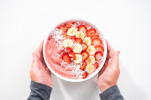 Disposizione piatta. Ciotola per frullato di fragole e banana guarnita con scaglie di cocco e frutta fresca.