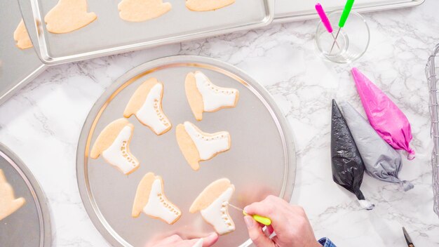 Disposizione piatta. Decorare i biscotti di zucchero a forma di pattino da ghiaccio con glassa reale di colore bianco.