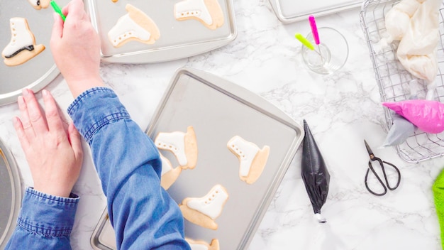 Disposizione piatta. Decorare i biscotti di zucchero a forma di pattino da ghiaccio con glassa reale di colore nero.