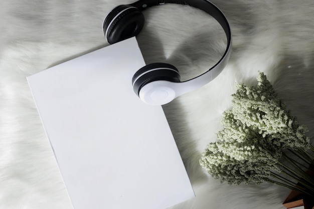 Disposizione piatta del libro e cuffie wireless con decorazioni floreali e sfondo piumato per il mock up