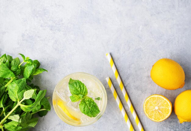 Disposizione piatta della bevanda alla limonata con limoni freschi Cocktail rinfrescanti con menta al limone e ghiaccio in vetro su sfondo testurizzato Concetto di bevande fredde estive Vista dall'alto e spazio di copia