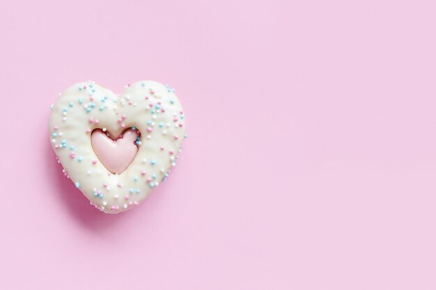 Disposizione piatta di due biscotti di panpepato a forma di cuore con granelli e glassa su sfondo rosa. Vista dall'alto della gustosa panetteria di San Valentino, panetteria fatta in casa per una vacanza romantica