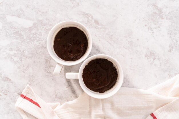 Disposizione piatta. Impasto per torta al cioccolato in coppette bianche pronte per essere sfornate.