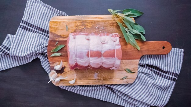 Disposizione piatta. Passo dopo passo. Arrosto di maiale disossato crudo sul tagliere di legno con le spezie.