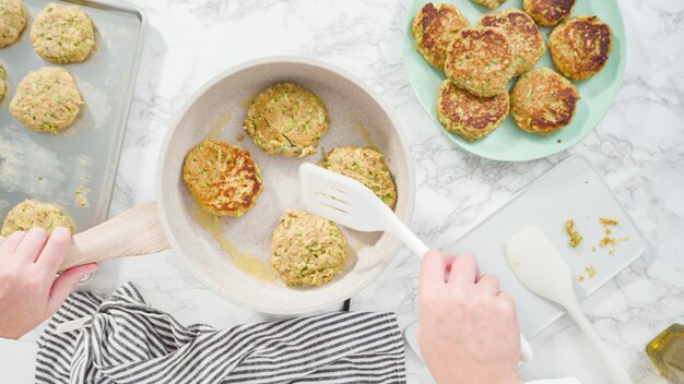 Disposizione piatta. Passo dopo passo. Friggere le torte di zucchine in olio d'oliva su una piccola padella.