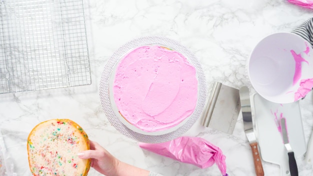 Disposizione piatta. Passo dopo passo. Glassa a strati di torta funfetti rotondi con glassa di crema al burro rosa.