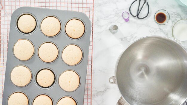 Disposizione piatta. Passo dopo passo. Raffreddamento di cupcakes alla vaniglia appena sfornati su una griglia di raffreddamento a filo.