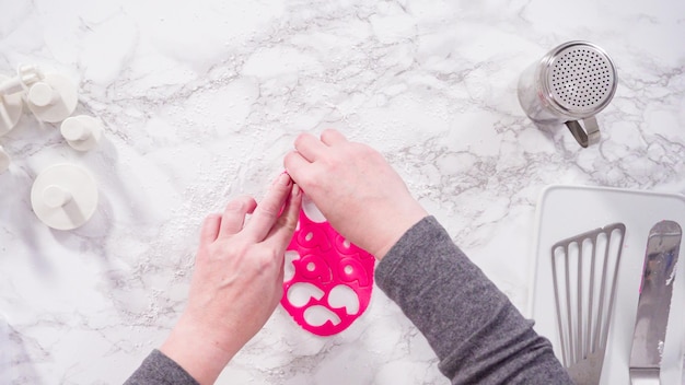 Disposizione piatta. Passo dopo passo. Tagliare i fiocchi di neve con le formine per biscotti dal fondente rosa su un bancone di marmo.