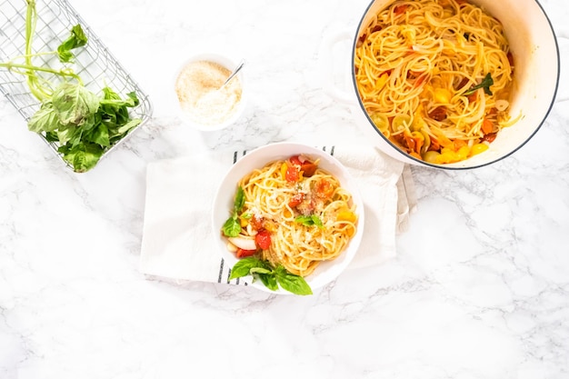 Disposizione piatta. Pasta vegetariana con pomodorini e basilico fresco su un piatto bianco.