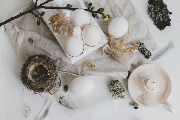 Disposizione piatta rustica di Pasqua Uova naturali piume rami di salice nidificano e candela su tavolo bianco invecchiato