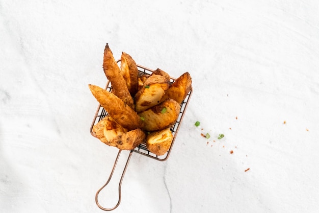 Disposizione piatta Spicchi di patate appena sfornati con spezie in un cestello di filo metallico