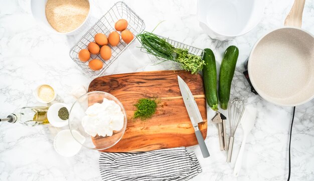 Disposizione piatta. Tagliare l'aneto fresco su un tagliere di legno per la ricetta delle torte di zucchine.