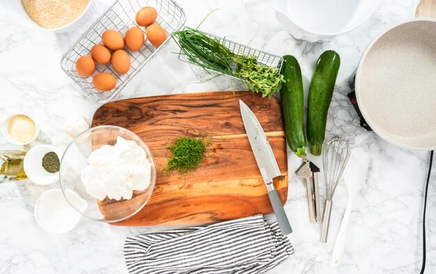 Disposizione piatta. Tagliare l'aneto fresco su un tagliere di legno per la ricetta delle torte di zucchine.