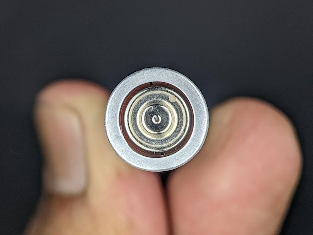 Dita del primo piano che tengono una batteria su uno sfondo nero