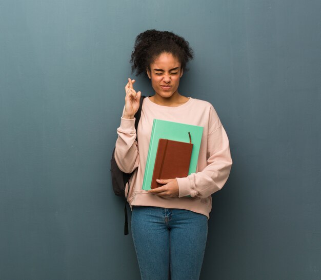 Dita dell'incrocio della giovane donna di colore dello studente per avere fortuna. Tiene dei libri.