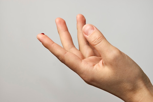 Dito della donna con una goccia di sangue per il test del diabete. Dito con goccia di sangue su sfondo bianco con copia spazio, close-up