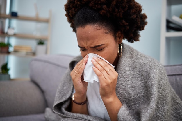 Divano malato e donna in una coperta con influenza a casa o appartamento con febbre fredda e naso soffiato Virus persona triste e di sesso femminile con un fazzoletto malato sul divano in un salotto con un problema medico