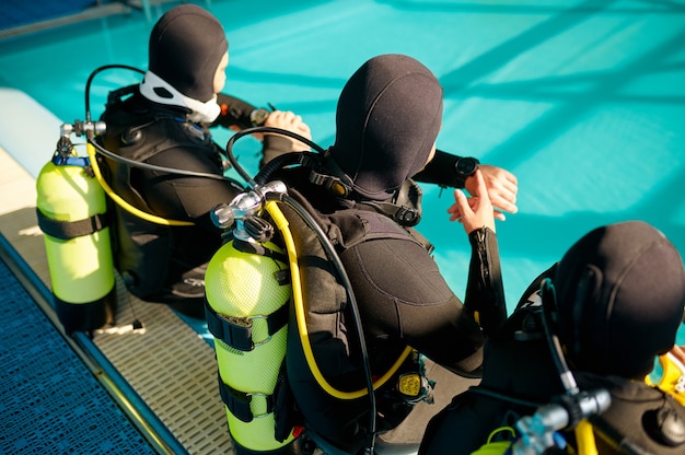 Divemaster e due subacquei in attrezzatura subacquea che si preparano per l'immersione, scuola di immersione. Insegnare alle persone a nuotare sott'acqua, interno della piscina coperta sullo sfondo