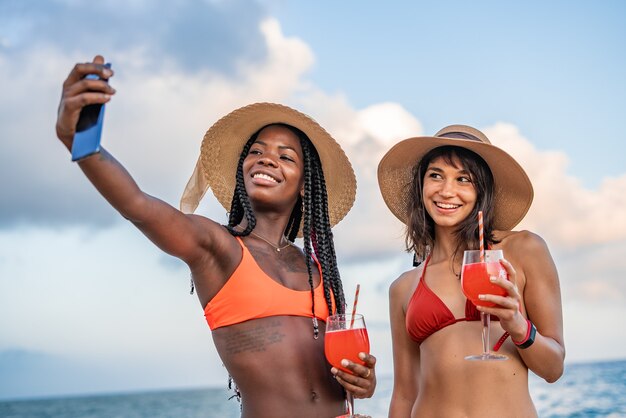 Diverse amiche che prendono selfie durante le vacanze estive sulla spiaggia