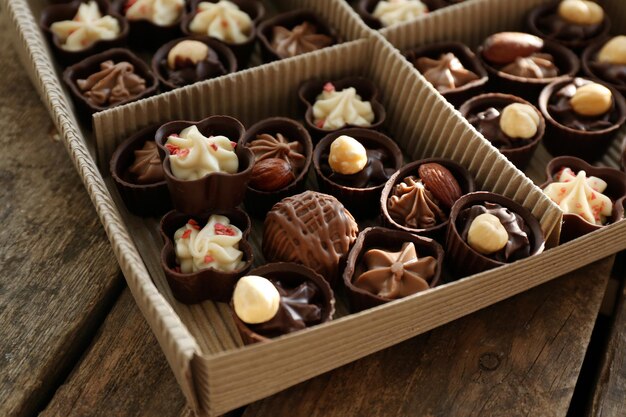 Diverse caramelle al cioccolato in scatola di carta su sfondo di legno, primi piani